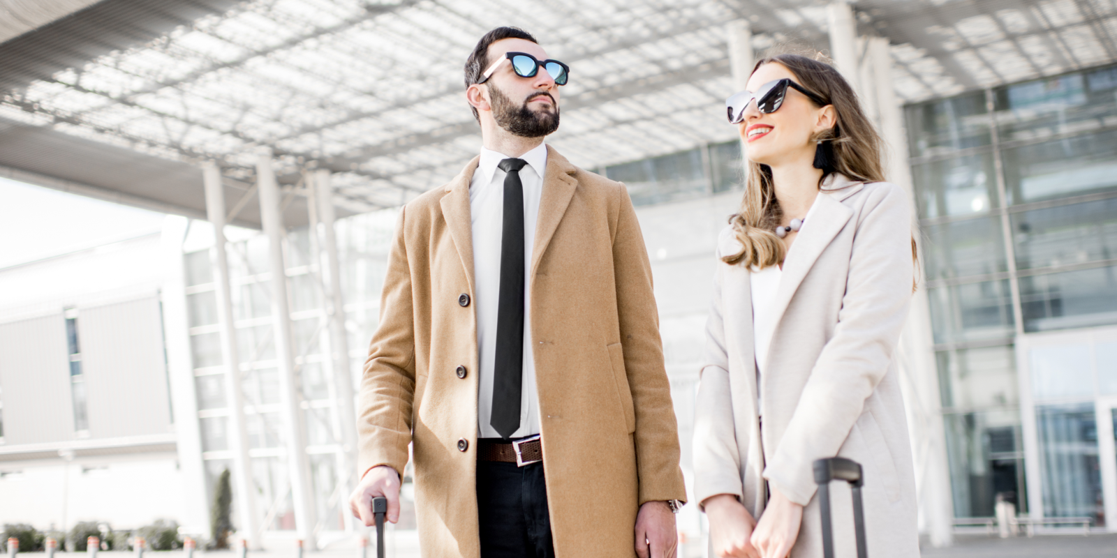 Pareja sonriente con maletas fuera de un aeropuerto