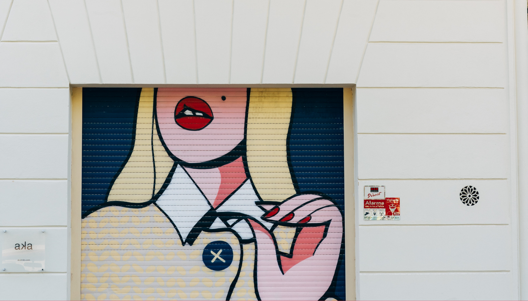 Grafiti de una mujer rubia con inspiración en el arte pop situado en la persiana metálica de un negocio.