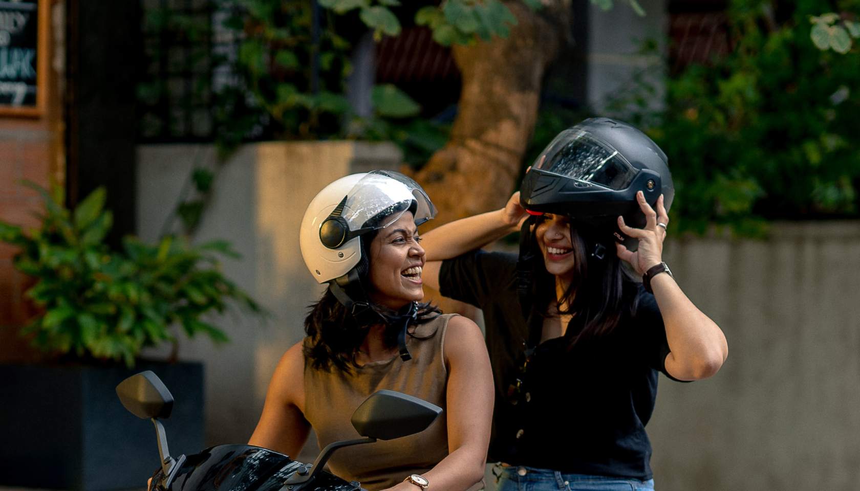 Dos chicas con cascos se ríen mientras utilizan una moto eléctrica.