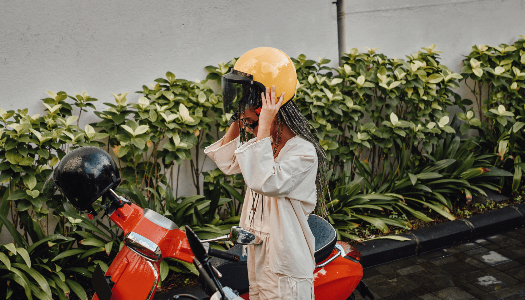 Chica joven se pone un casco amarillo en la cabeza al lado de una moto roja.