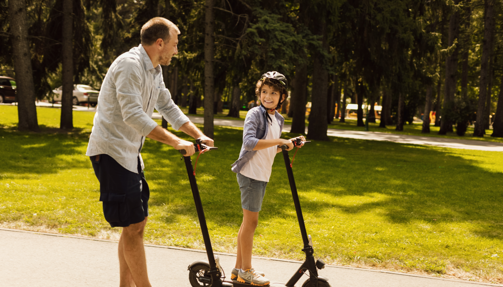 Padre e hijo paseando en patinete por un parque rodeado de árboles