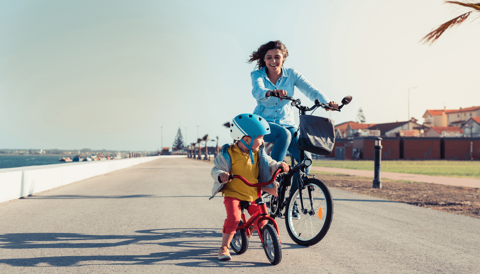 Madre e hijo se ríen y disfrutan de un trayecto en bicicleta por un paseo marítimo.